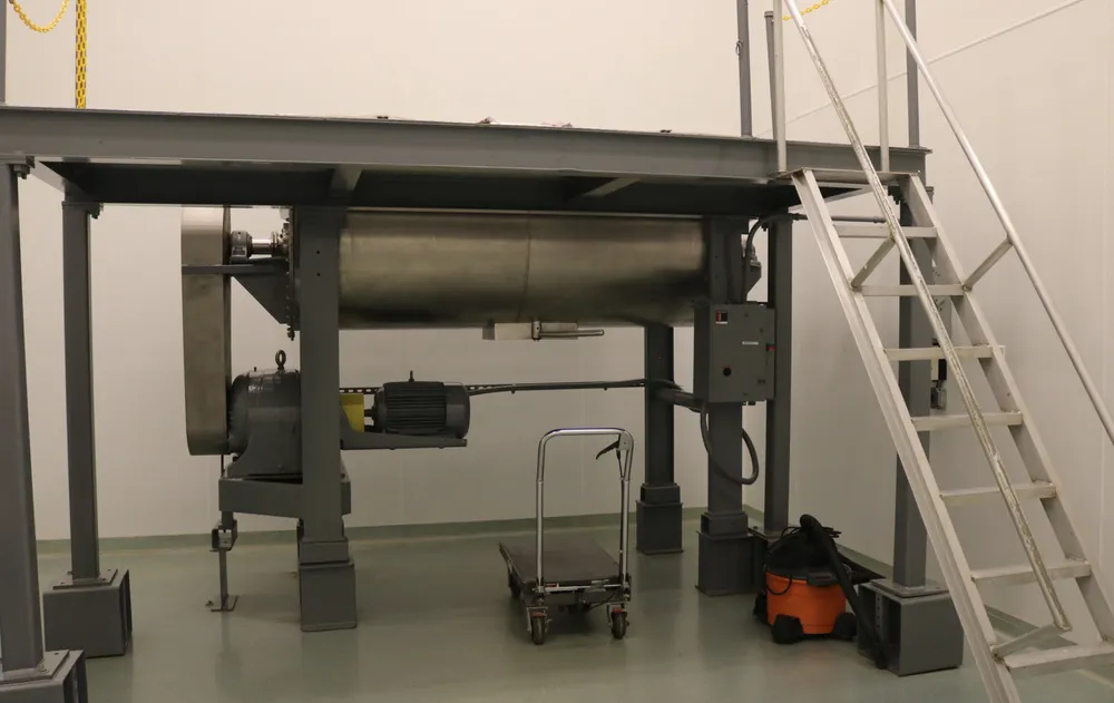 A large industrial mixer stands in a supplement manufacturing room, accompanied by a ladder for easy access to higher areas